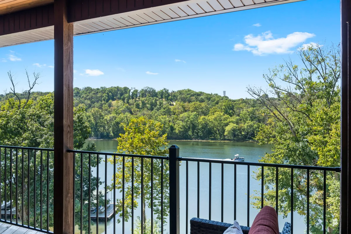 This exterior shot showcases a wide lake view lined with green trees and beneath a clear blue sky. The tranquil mood invites thoughts of fishing, boating, or simply relaxing while watching the sunrise or sunset over the lake.