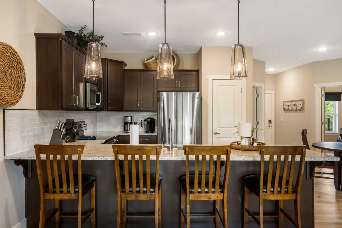 The photo presents a kitchen island with comfortable seating, pendant lights, and visible modern appliances, offering a warm and welcoming environment ideal for both cooking and casual dining. Decorative accents add a homey touch.