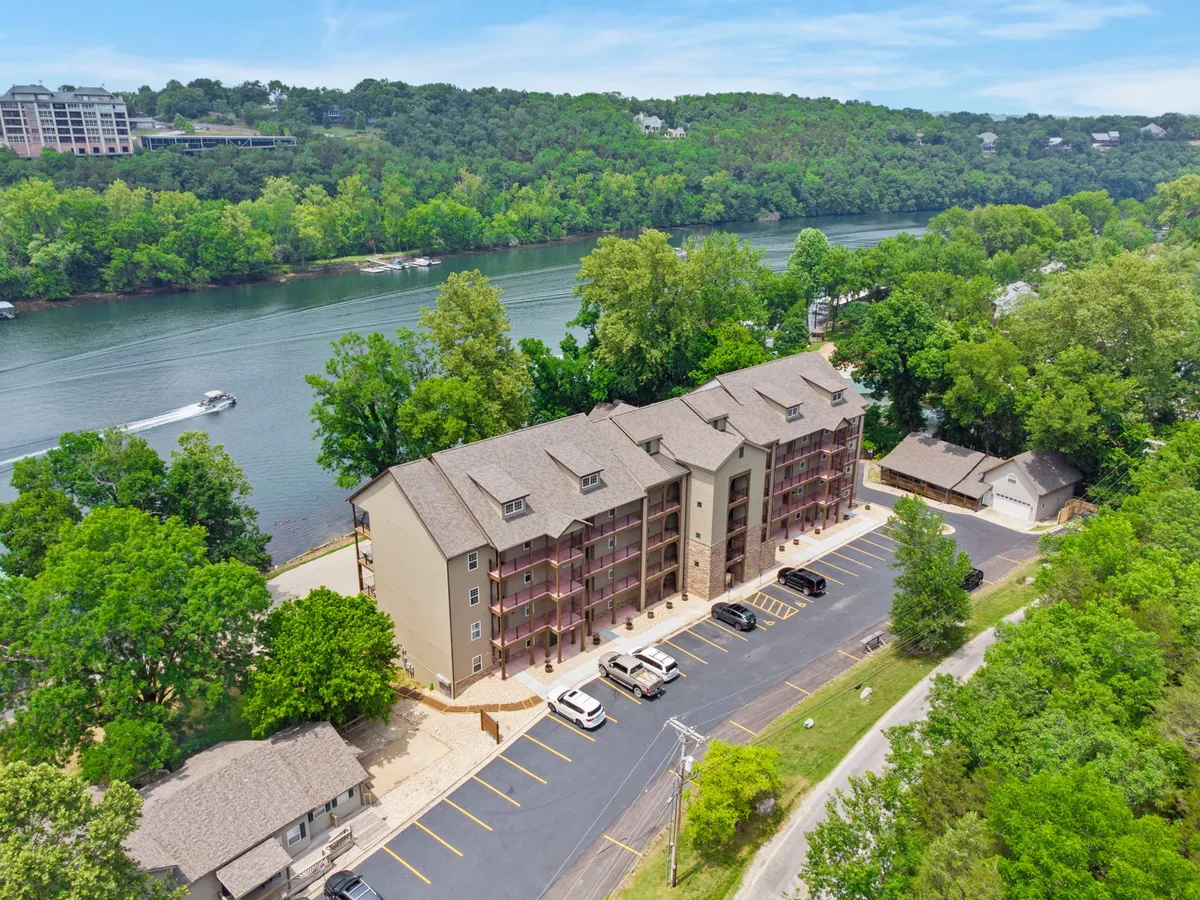 A calm exterior view overlooking a river, with a building nestled among leafy green trees and a parking area visible nearby. The scene exudes tranquility, with the river inviting activities such as boating, fishing, or simply relaxing by the water. The natural surroundings showcase lush foliage and the opportunity for wildlife spotting.