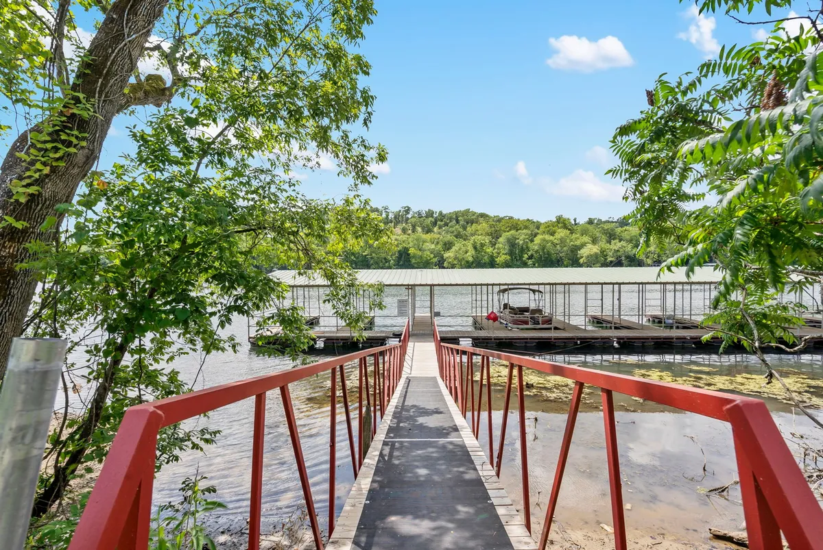 A picturesque exterior scene featuring a distinctive red bridge crossing the waterfront, with docks and leafy trees flanking calm water. The image suggests both recreational opportunities and scenic beauty, encouraging exploration along the shoreline.